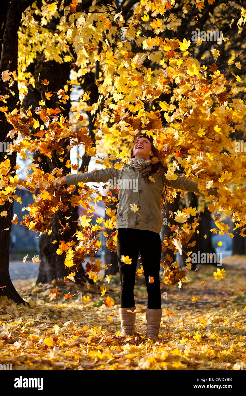A beautiful young woman smiling throws orange leaves into the air surrounded by fall colors in Idaho. Stock Photo