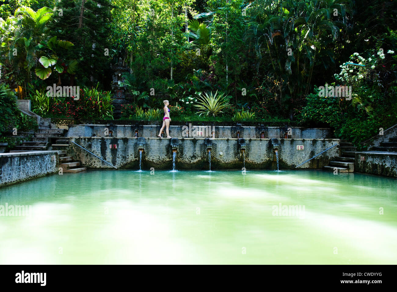 A beautiful woman relaxing next to a hot springs surrounded by a lush jungle and flowers in Bali, Indonesia. Stock Photo