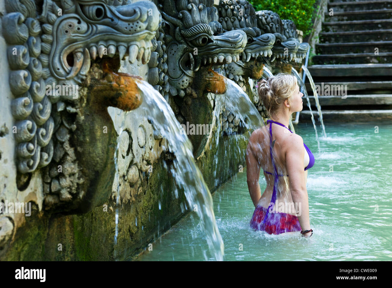 A beautiful woman relaxing in a hot springs surrounded by a lush jungle and flowers in Bali, Indonesia. Stock Photo