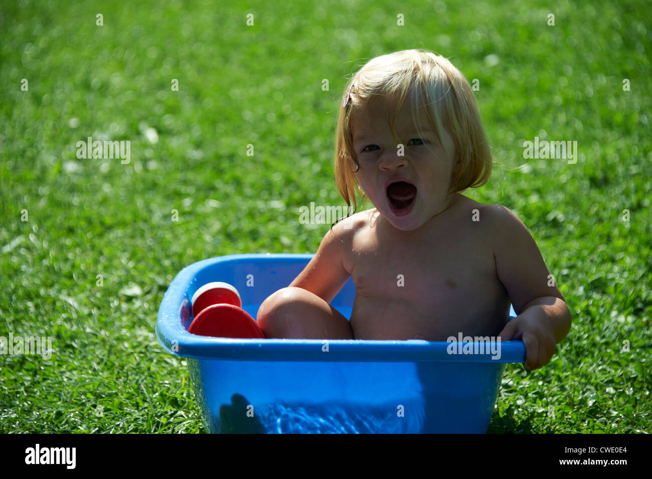 Child Baby girl having a bath in blue bathtub, outside, garden, sunny