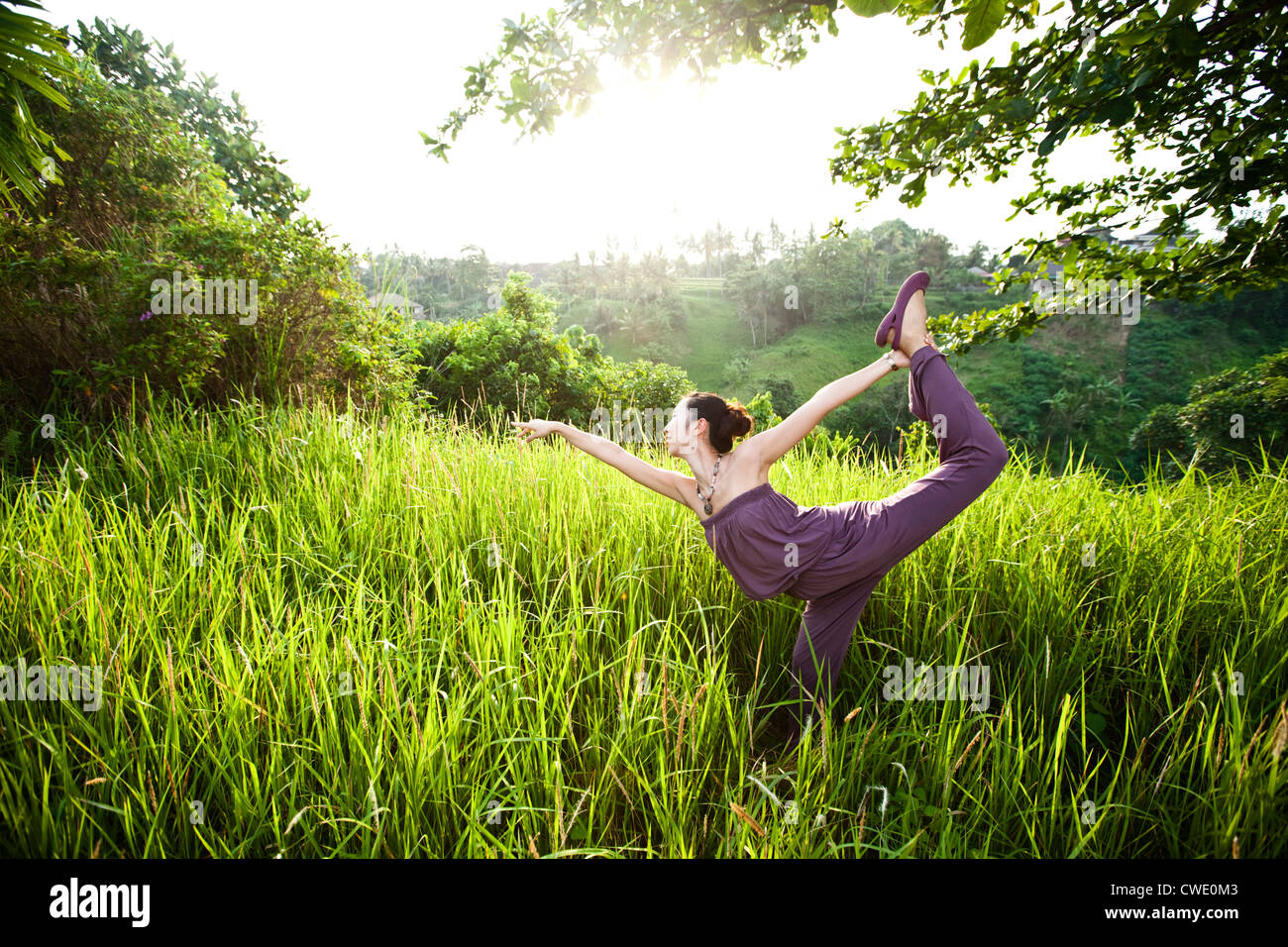 A athletic woman practing yoga in a lush field in Bali, Indonesia. Stock Photo