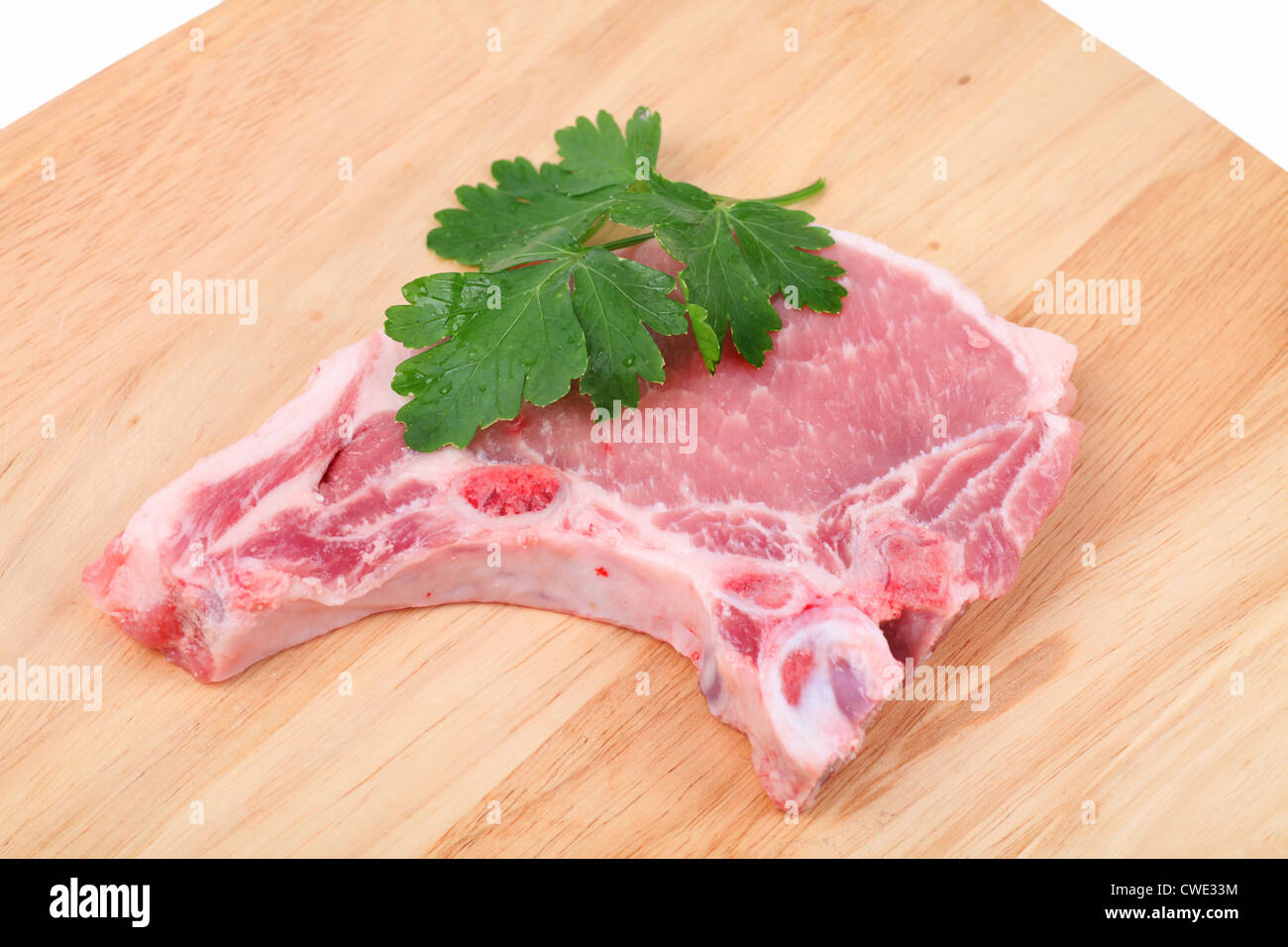 Pork chop and a leaf of parsley on a cutting board. Stock Photo