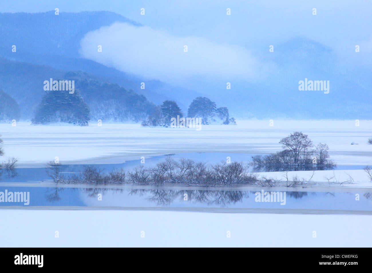 Frozen Lake And Smoke Rising From Lower Mountains In Background Stock Photo