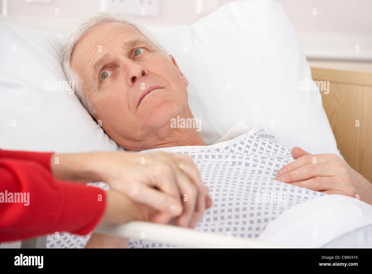 Senior man in hospital bed holding wife's hand Stock Photo