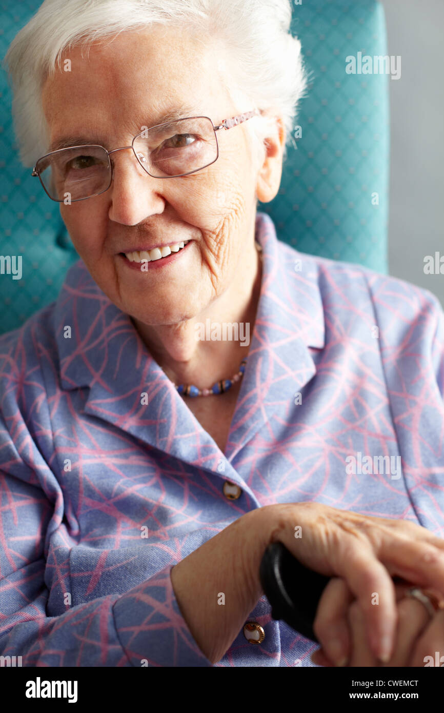 Senior Woman Relaxing In Chair Holding Walking Stick Stock Photo