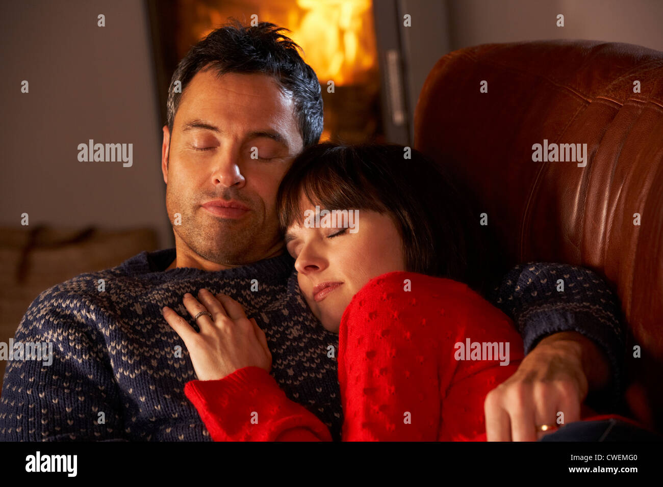 Middle Aged Couple Cuddling On Sofa By Cosy Log Fire Stock Photo Alamy