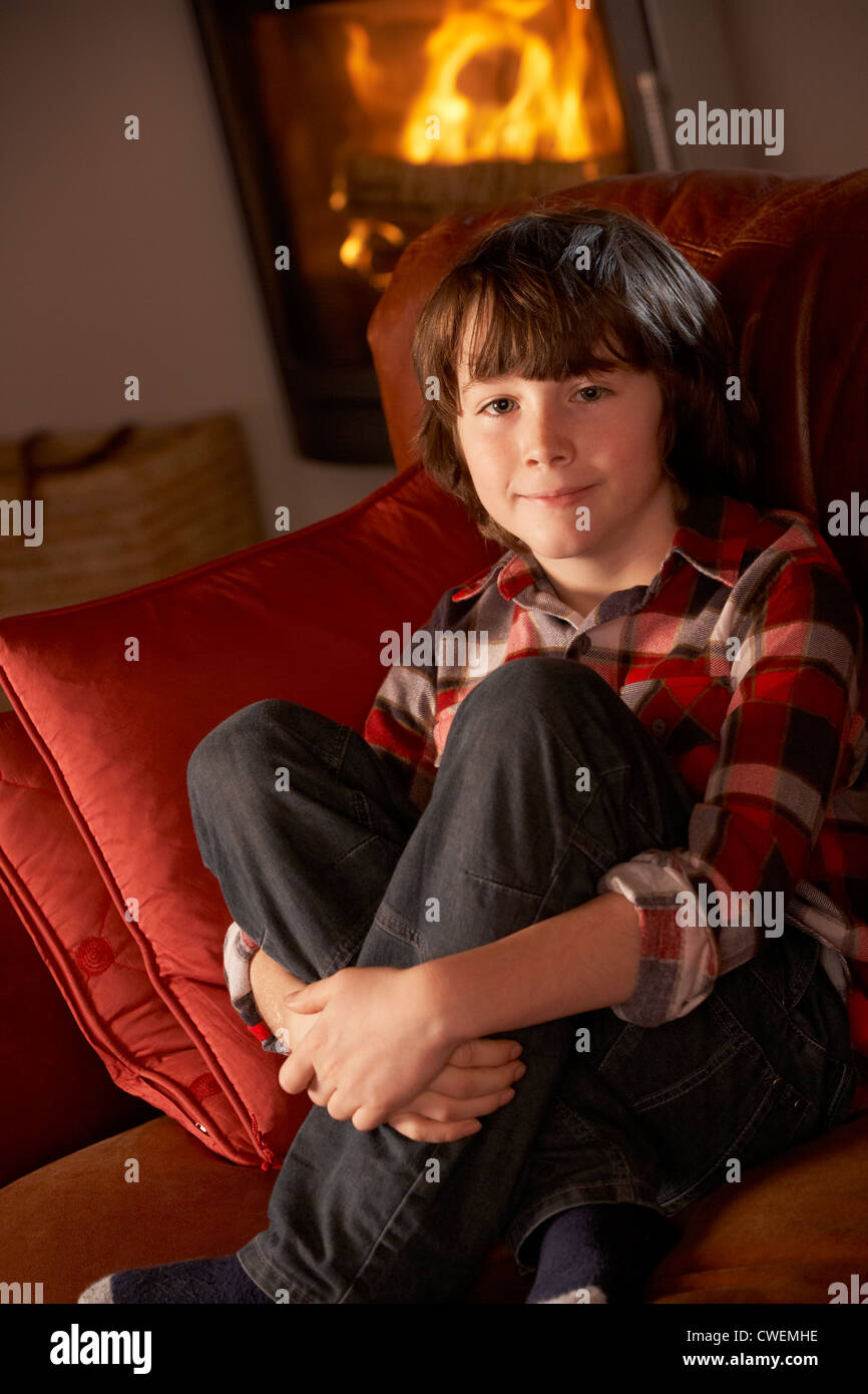 Young Boy Sitting On Sofa By Cosy Log Fire Stock Photo - Alamy