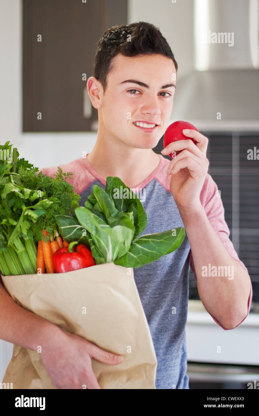 Handsome young man holding a bag of organic groceries eating a red apple Stock Photo