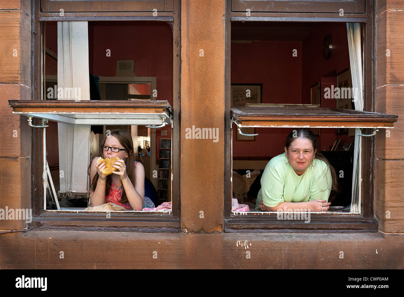 Mother and daughter looking out the window of their flat, Howat Street,Govan, Glasgow, Scotland, UK Stock Photo