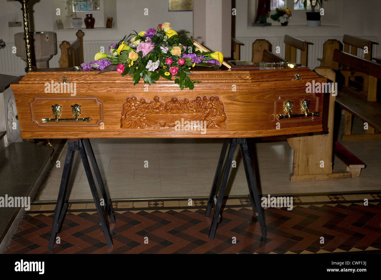 A wooden coffin with last supper design and flowers on top resting in church ready for the occupant's funeral the following day Stock Photo