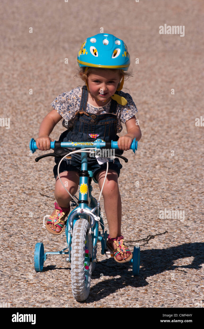 Little Girl Child Riding a Bike with stabilisers wearing a safety helmet Stock Photo