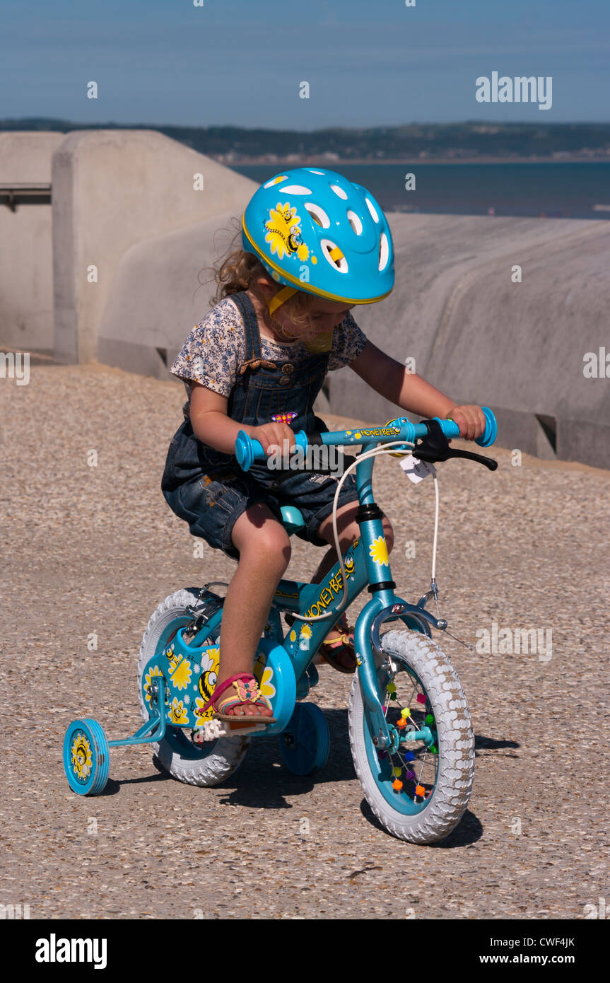 Little Girl Child Riding a Bike with stabilisers wearing a safety