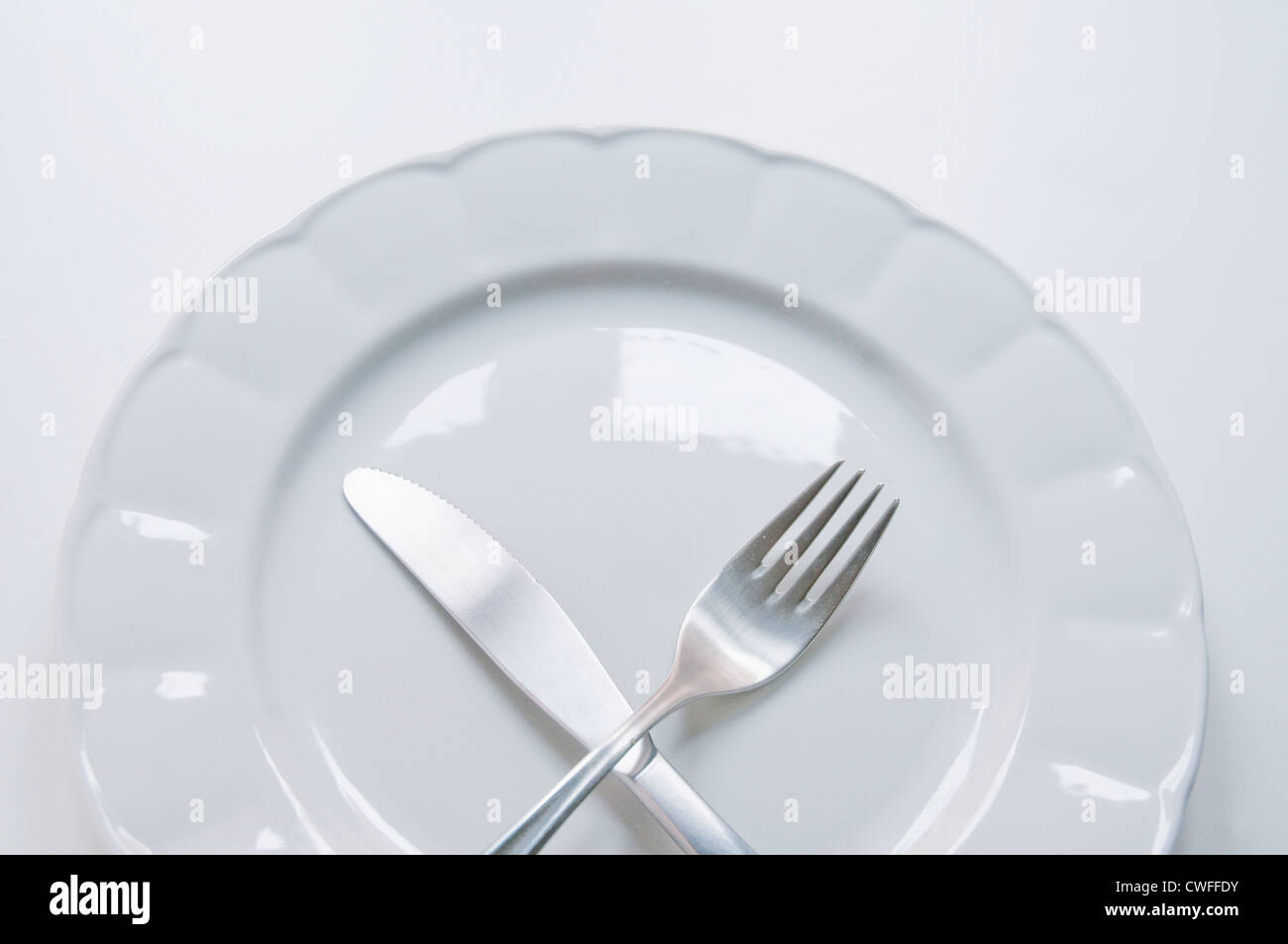 Crossed fork and knife on an empty plate. Stock Photo