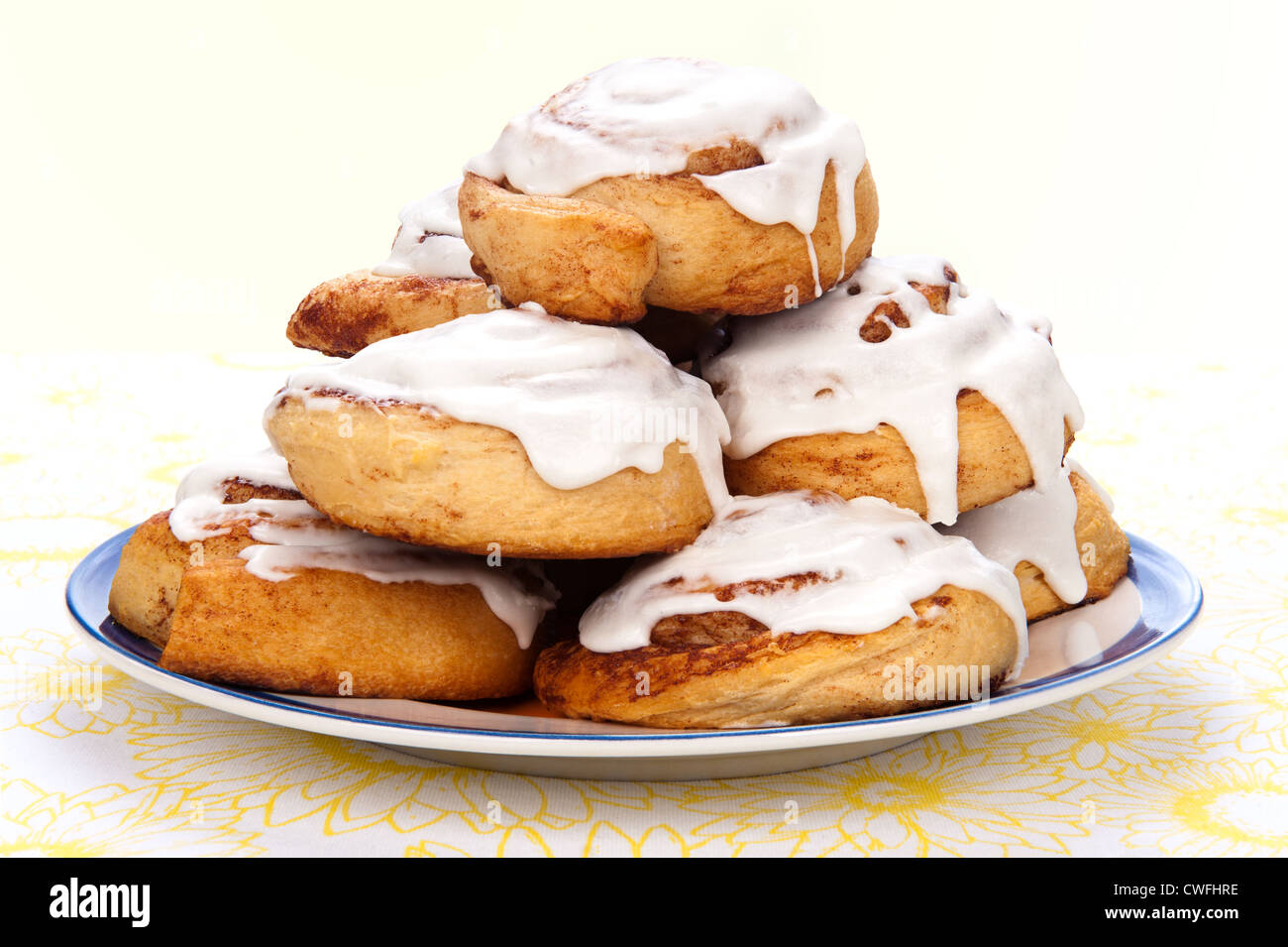 A plate of freshly baked cinnamon rolls with sweet, white icing dripping down the sides. Stock Photo