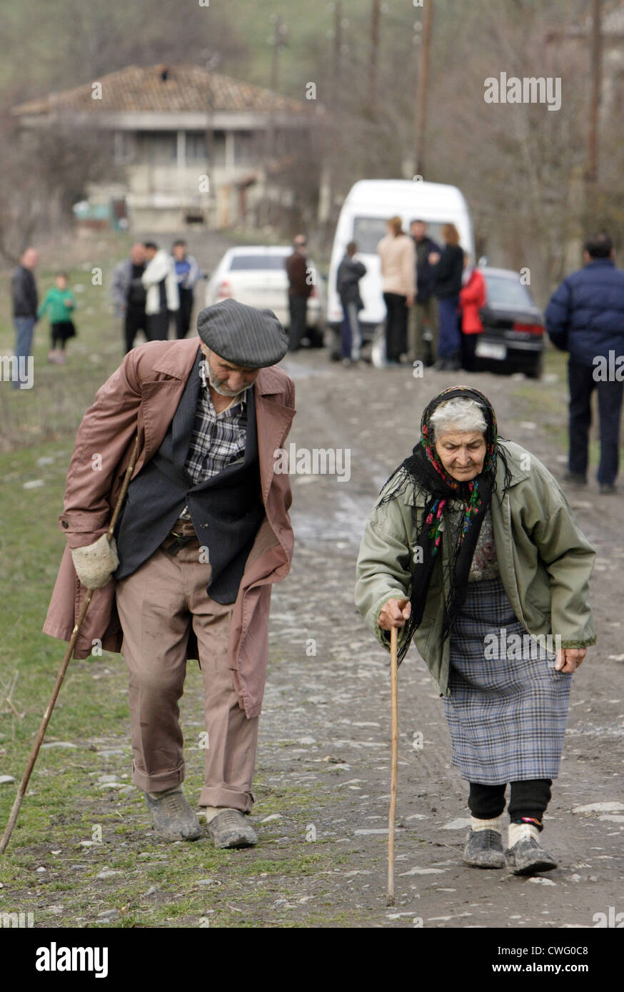 An old woman and an old man walk hunched over on a rural road Stock