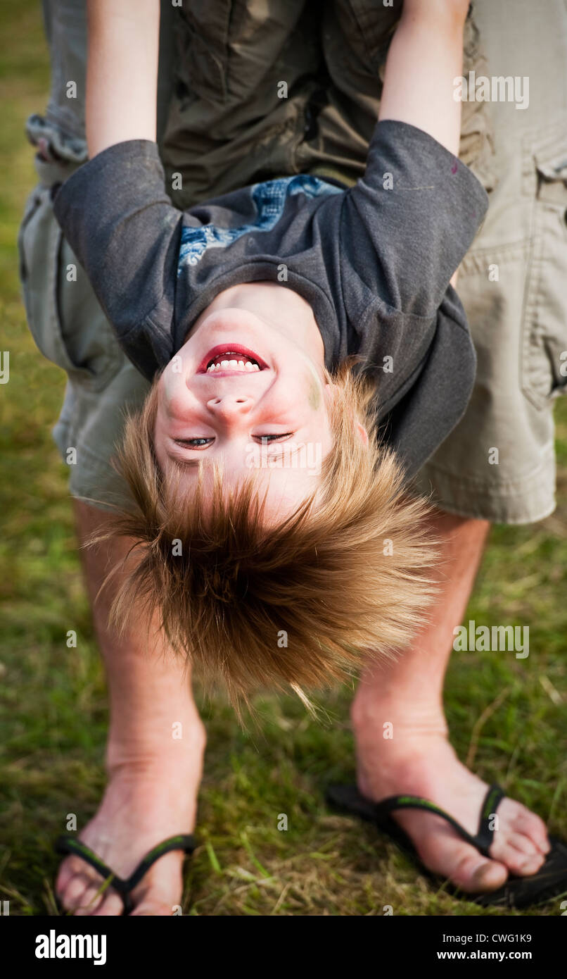 A laughing boy being swung upside-down by his father at Wilderness music festival, Cornbury, Oxfordshire, UK Stock Photo