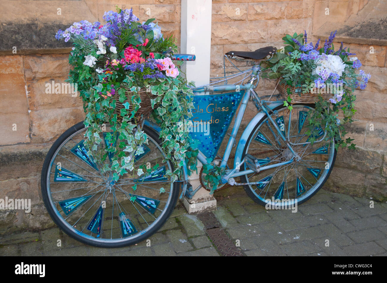 Bicycle decorated with flowers outside Jola Glass Studio on Lower High Street Chipping Campden Goucestershire Cotswolds England Stock Photo