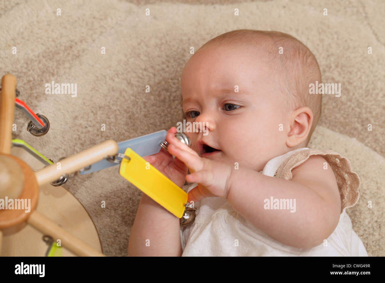 A 6 month old baby girl laying on a baby blanket and playing with a mobile Stock Photo
