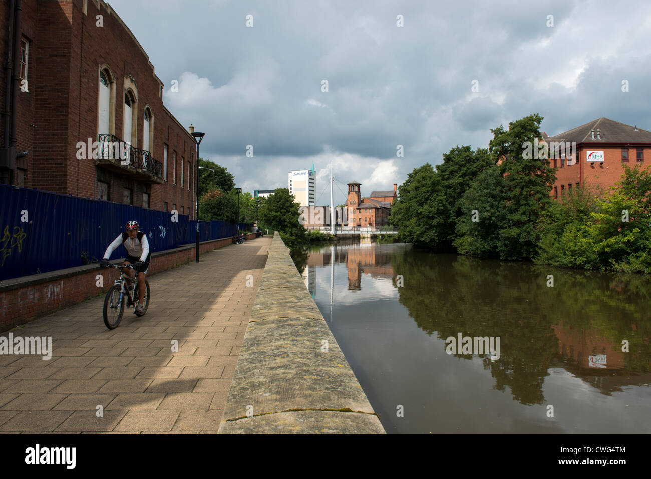 Cyclist riding along riverside path in Derby with the Silk Mill Industrial Museum and Jurys Inn in the background Stock Photo