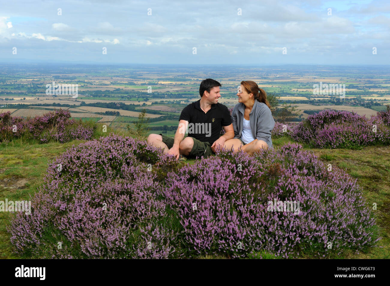 Smiling couple sitting by the heather on Wrekin Hill in Shropshire England Uk Stock Photo