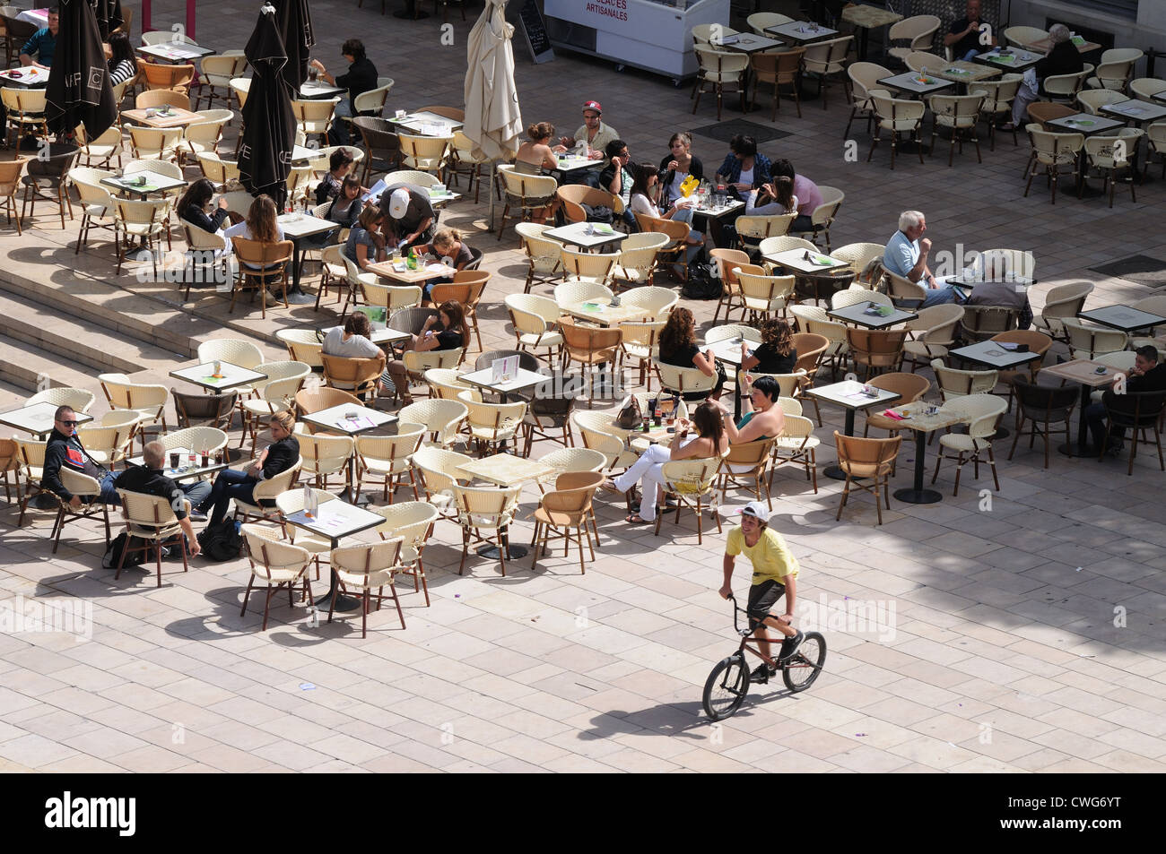 Boy cyclist riding past outdoor tables of Cafe Carree in Nimes France Stock Photo