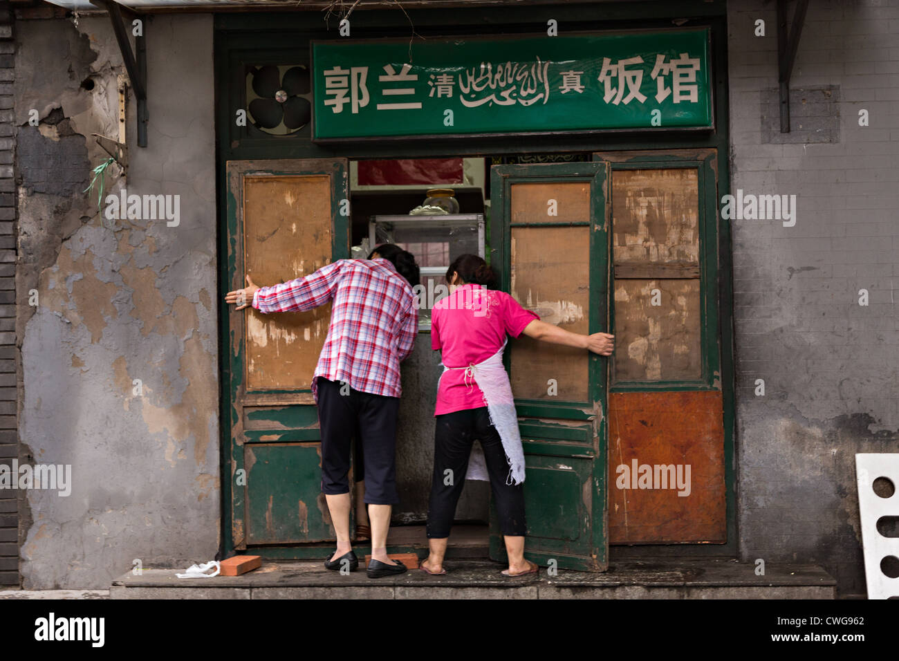 Two women close up their traditional shop along a hutong in Beijing, China Stock Photo
