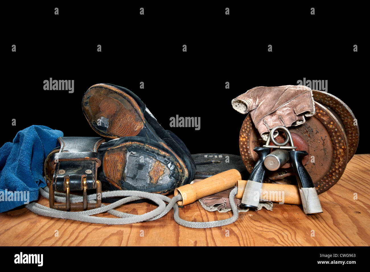 A collection of old exercise equipment including hand grips, dumbell, jump rope and old, torn weightlifting shoes. Stock Photo