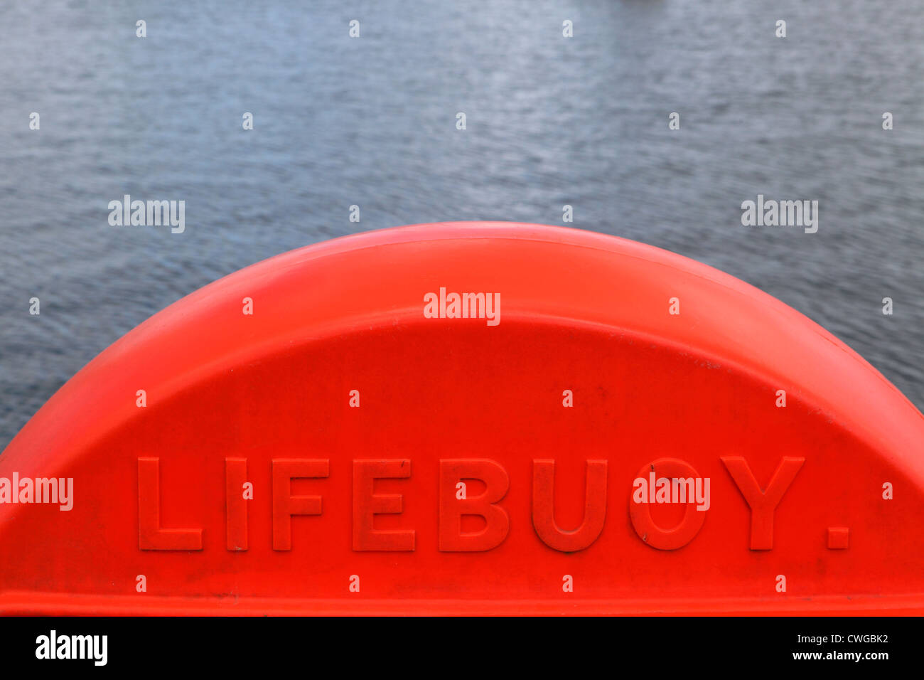 Bright orange red plastic Lifebuoy container on waterfront with calm sea behind. Bright colorful, safety equipment, Cornwall, UK Stock Photo