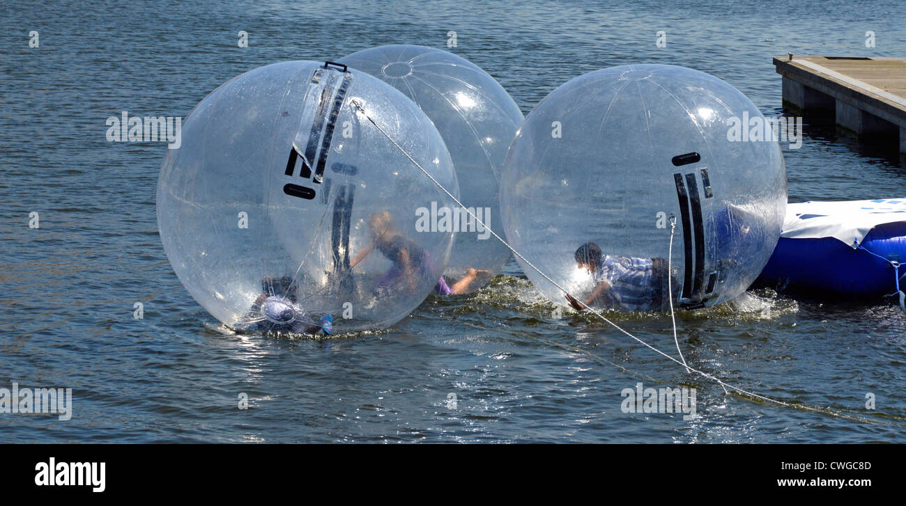 Kids playing inside tethered inflatable bubbles on dock water at Aqua Balls facility with minders (out of shoot) in attendance Stock Photo
