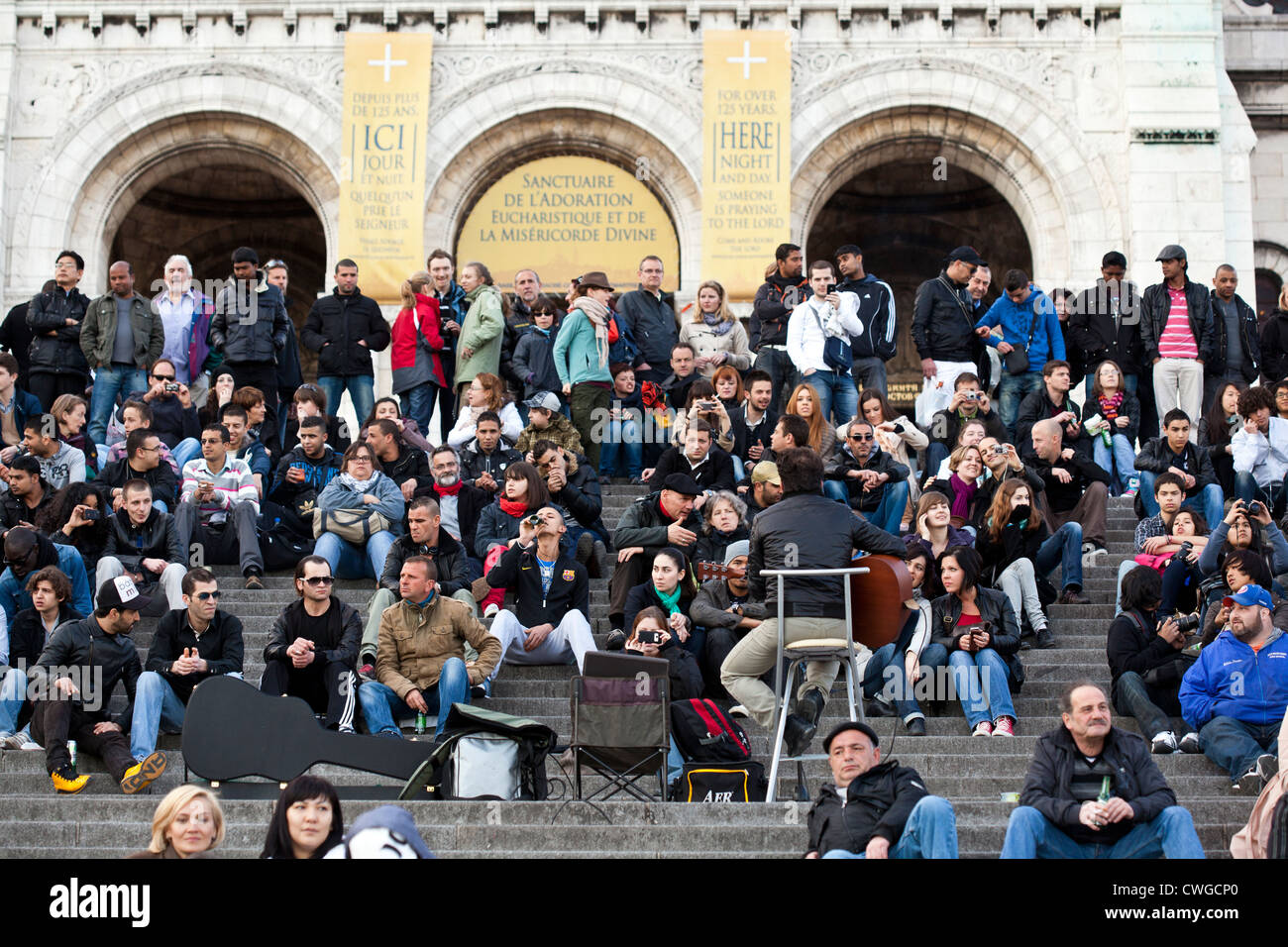 A crowd of tourists listen to a musician perform on the steps of the Sacre Couer, Paris. Stock Photo