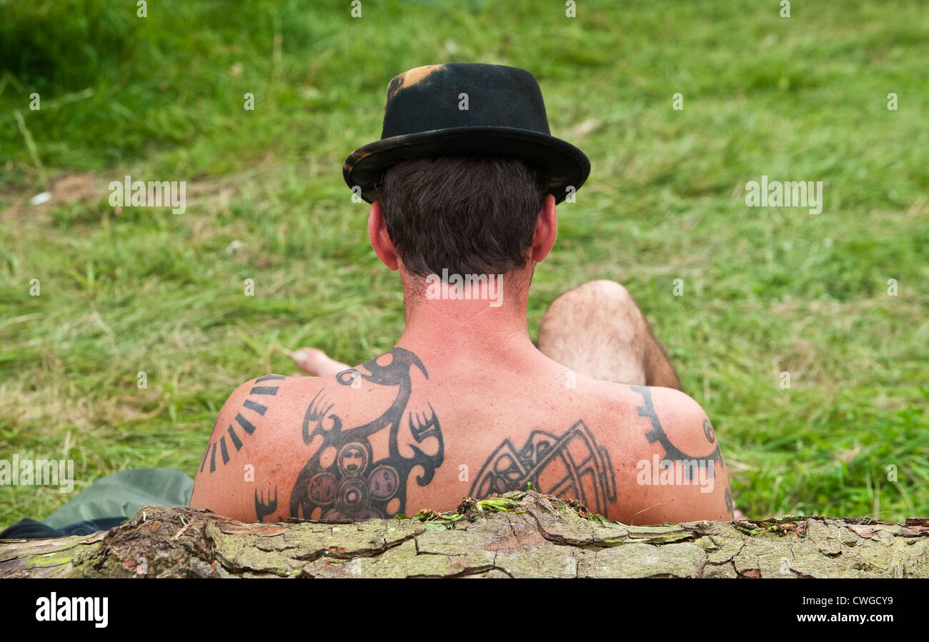 A festival goer bares his tattooed back while relaxing at the Wilderness music festival, Cornbury, Oxfordshire, UK Stock Photo