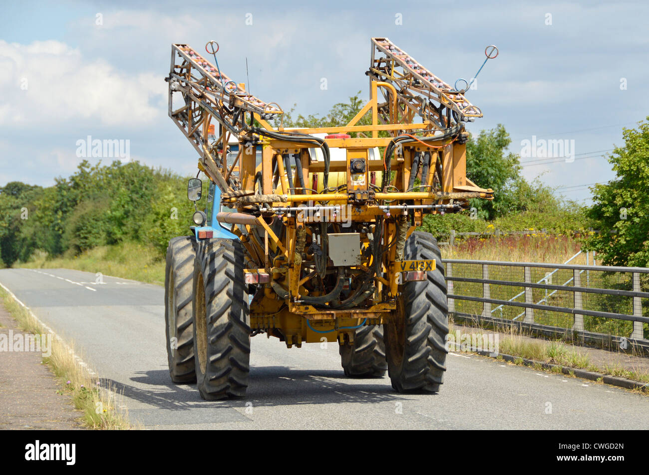 Crop spraying equipment mounted on wide tractor travelling along narrow