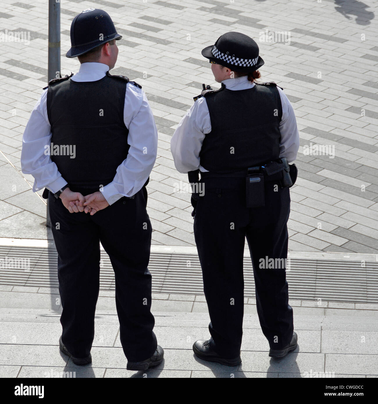 Back view male & female Metropolitan police officers in uniform outside Stratford train & bus stations from steps to Westfield shops at East London UK Stock Photo