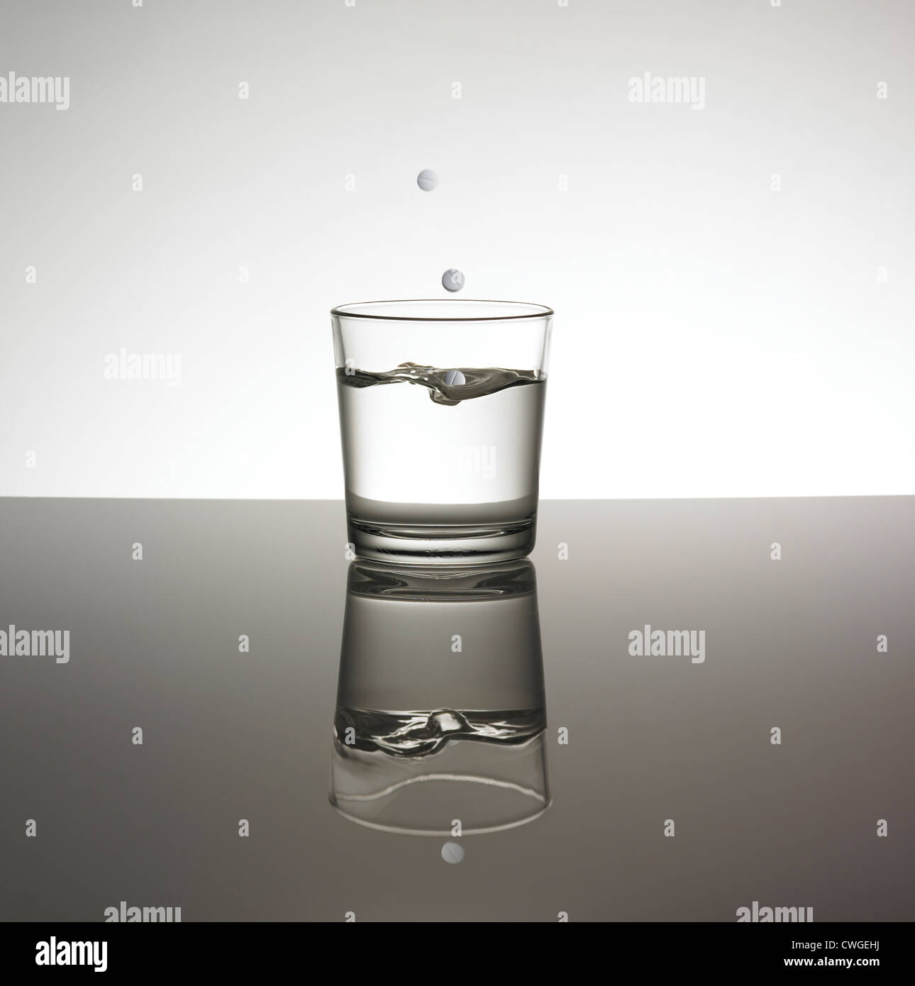 Tablets dropping in glass on water creating a splash on a reflective