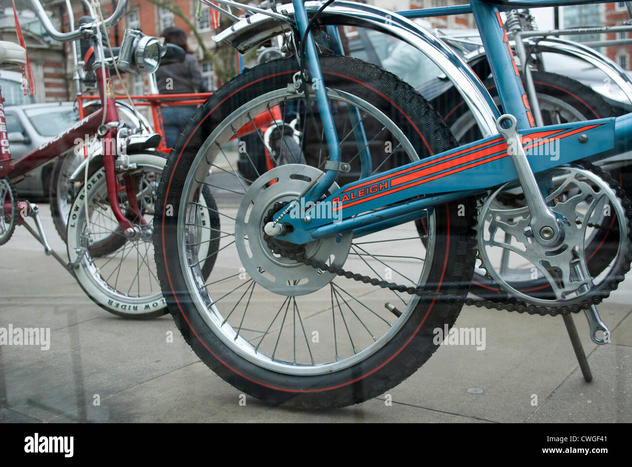 Rear wheel of a Raleigh Chopper and other bicycles outside Tate Britain seen through clear barrier Stock Photo