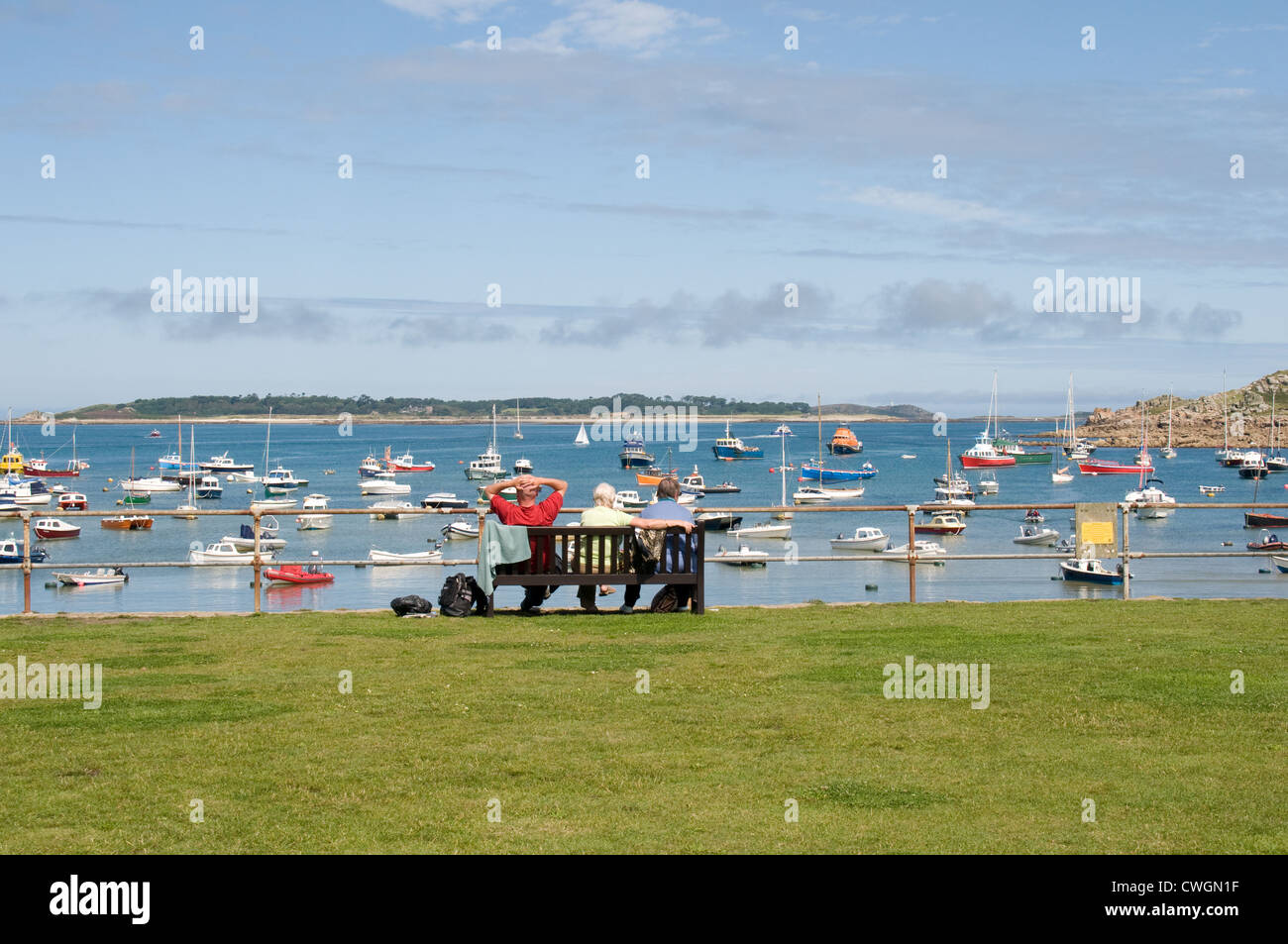 A group of people relax on a seat enjoying the view over Hugh Town Harbour , St Mary's, Isles of Scilly Stock Photo