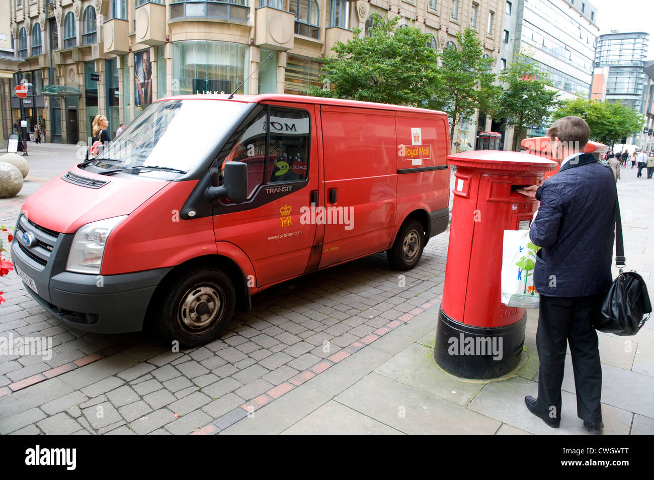 man posting mail in a royal mail post box with a royal mail van parked beyond 2012 Stock Photo