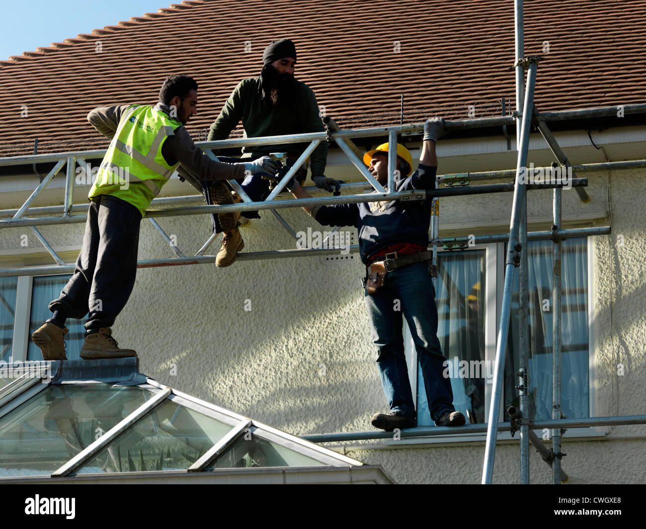 Sikh Workmen Putting Up Scaffolding Around A House England Surrey Stock Photo