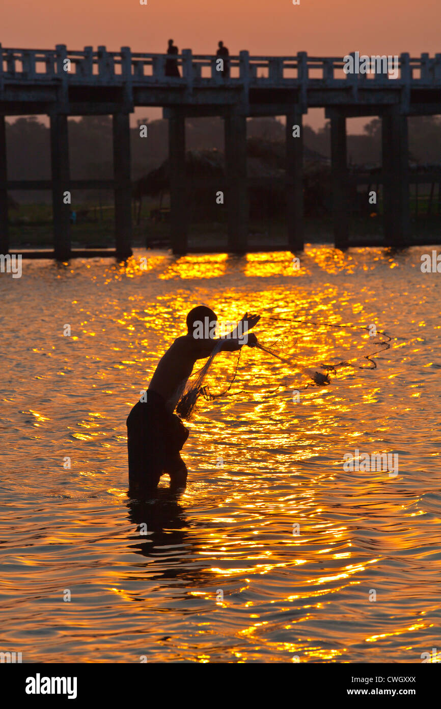 A FISHERMAN casts his net below U BEINS BRIDGE on Taungthaman Lake at sunrise - AMARAPURA, MYANMAR  Stock Photo