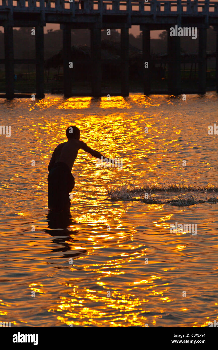 A FISHERMAN casts his net below U BEINS BRIDGE on Taungthaman Lake at sunrise - AMARAPURA, MYANMAR Stock Photo
