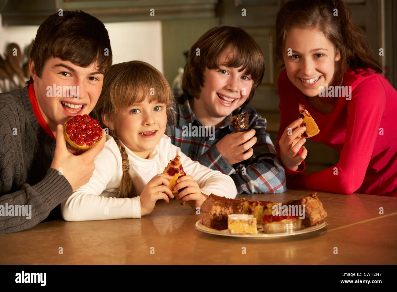 Group Of Children Enjoying Plate Of Cakes In Kitchen Stock Photo