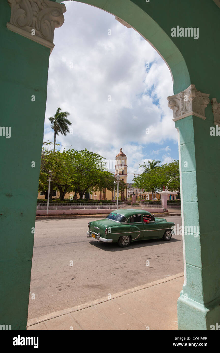 A vintage old antique 1950s car and Iglesia Mayor de San Juan Bautista church from archway in Remedios, Cuba. Stock Photo