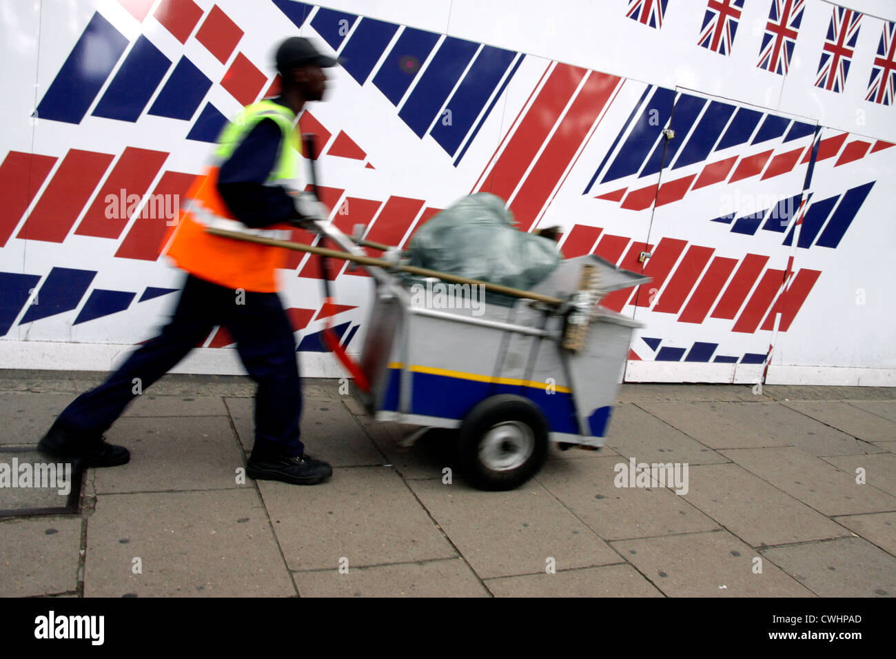 Street cleaner pushing his dust cart past a large Union flag in central London Stock Photo
