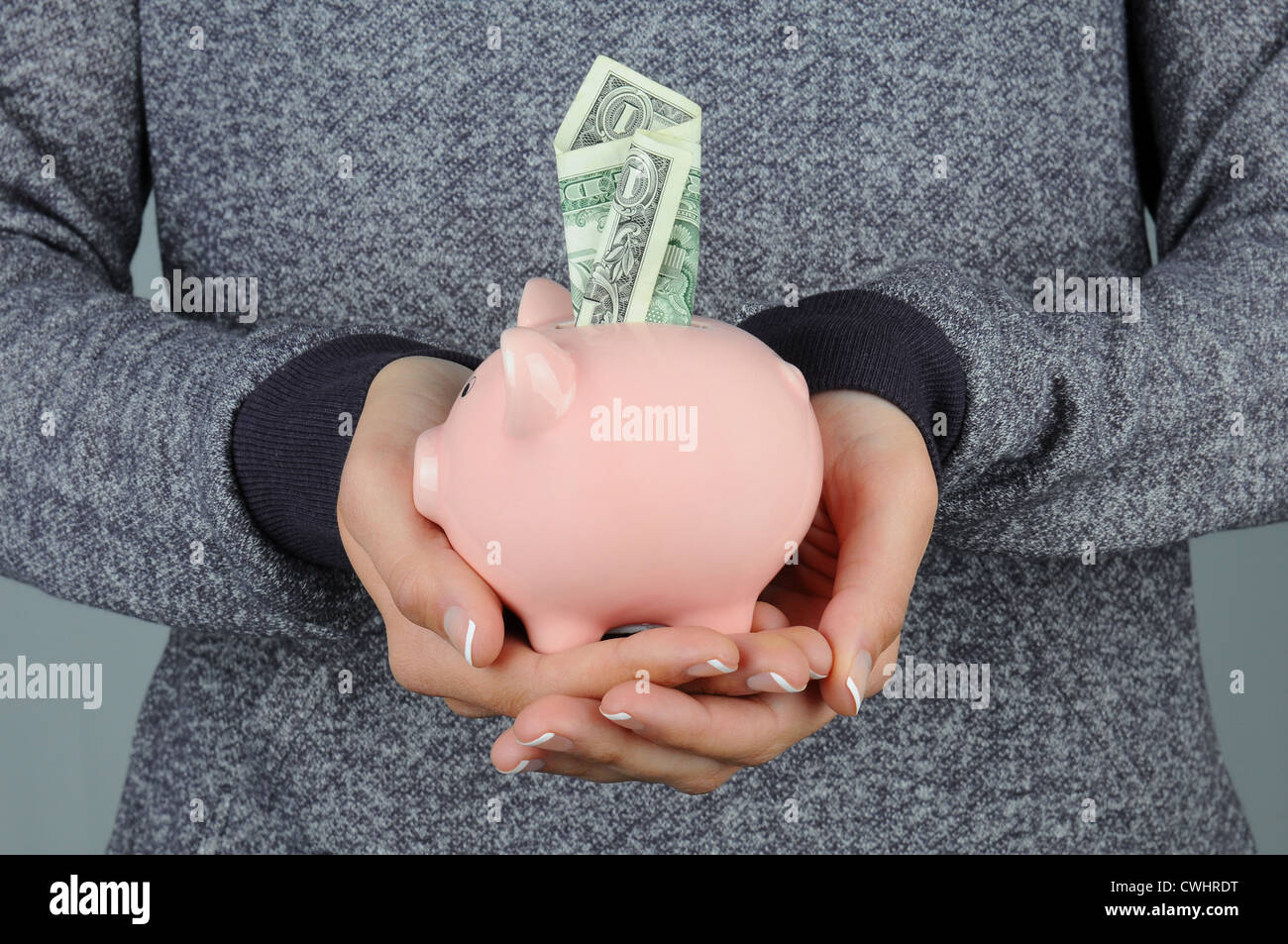 Closeup of a woman holding a piggy bank in front of her body. Bank has a dollar bill sticking in the top slot. Stock Photo