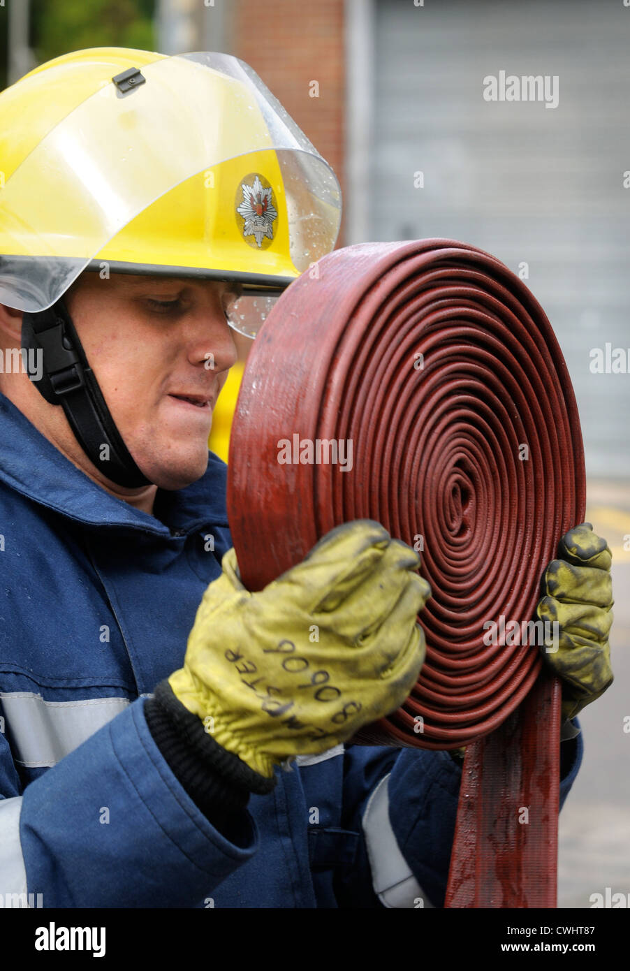 A fireman coiling up a hose during an exercise with white watch at Pontypridd Fire Station in South Wales UK Stock Photo