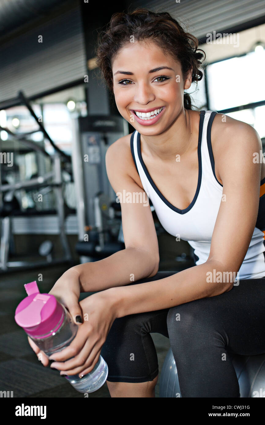 Mixed race woman drinking water in health club Stock Photo