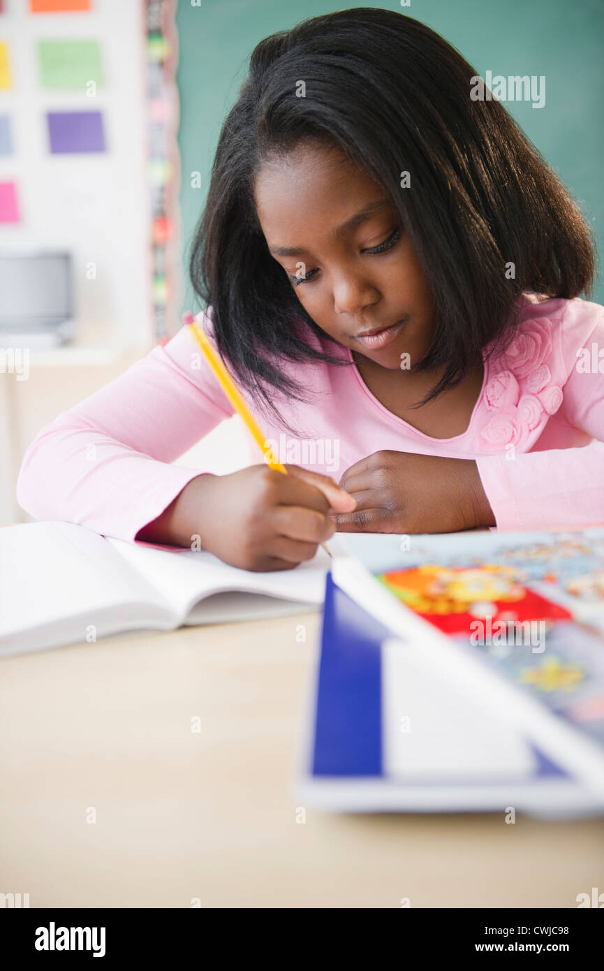 Black student writing in notebook in classroom Stock Photo