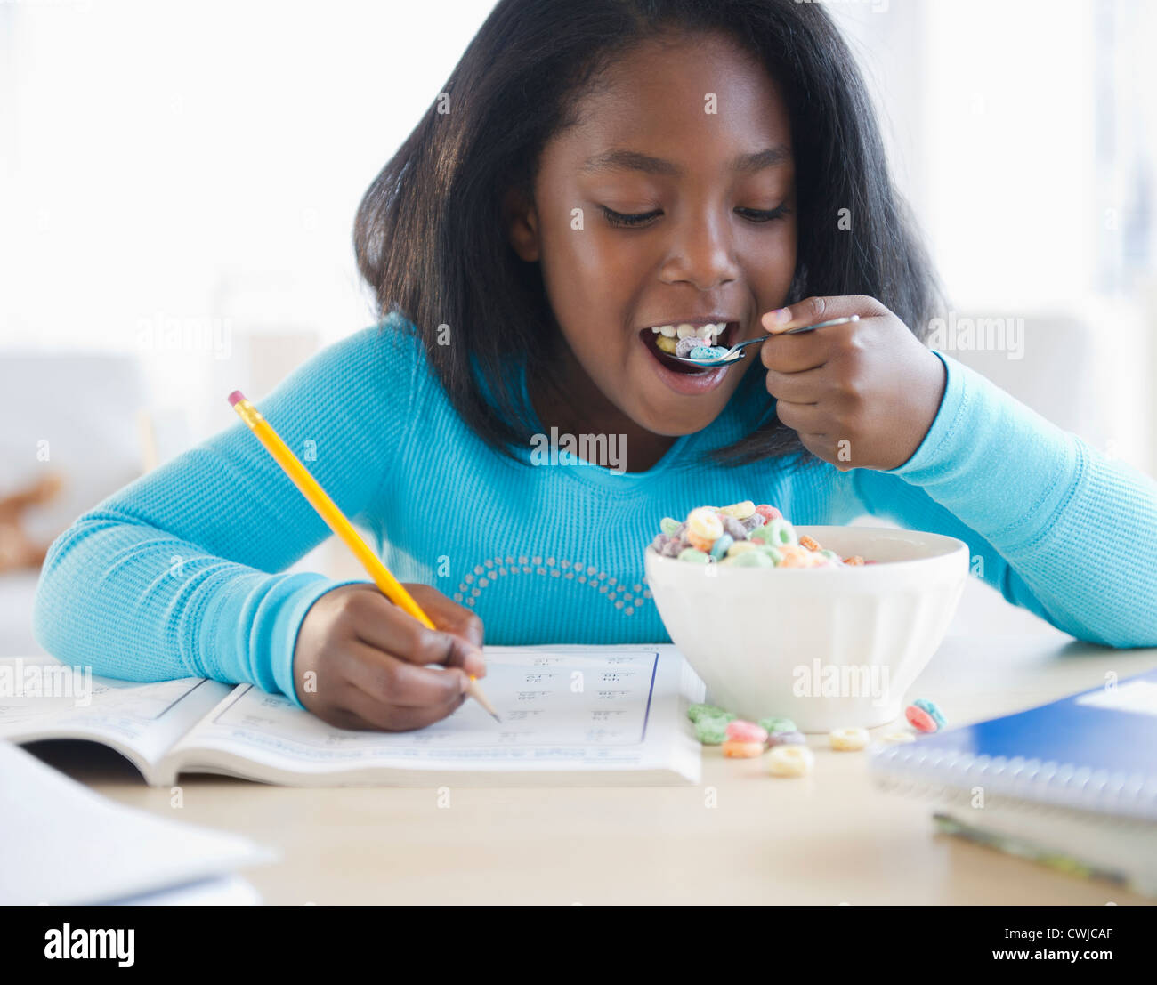 Black girl eating cereal and writing in workbook Stock Photo