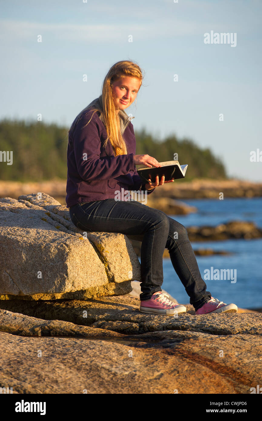 Young woman with journal at sunset, Schoodic Peninsula, Maine, USA Stock Photo