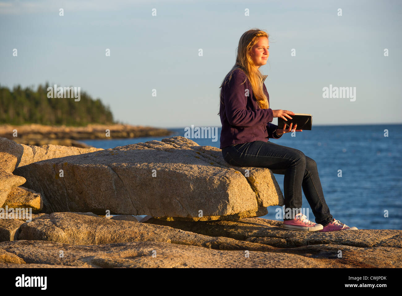 Young woman with journal at sunset, Schoodic Peninsula, Maine, USA Stock Photo